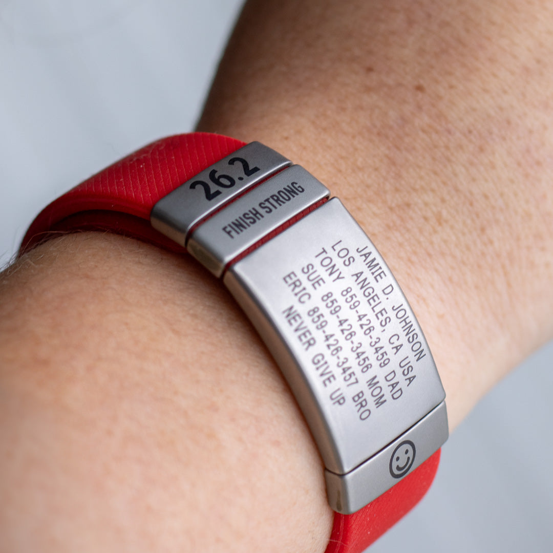 Red and silver ROADiD with engraved text on a wrist against a neutral background