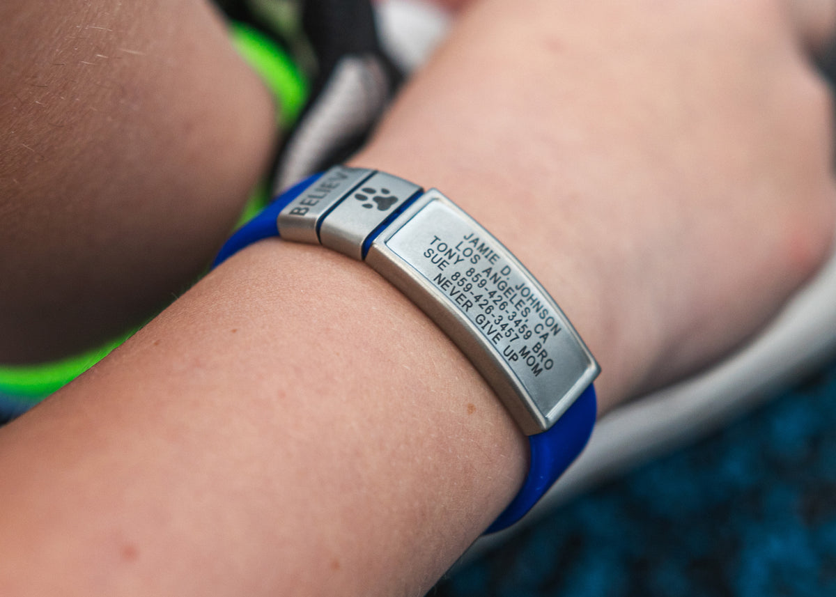 Close up of kid wearing a blue and slat ROADiD Kids Stretch ID with engraved text on a blurred background
