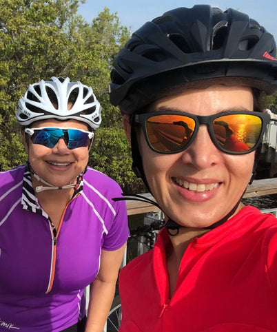 Two people wearing cycling helmets and sunglasses with a scenic background.